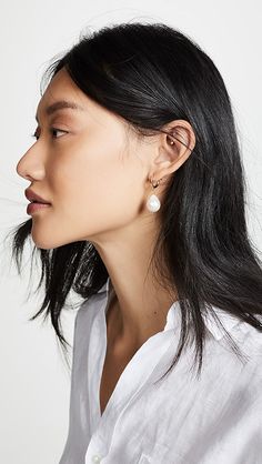 a woman with long black hair wearing white shirt and gold earring on her left ear