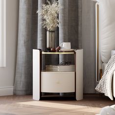 a white table with a vase and some books on it next to a window curtain