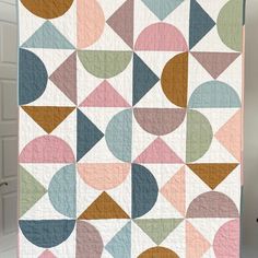 a quilt hanging on a clothes line with an abstract design in pastel colors and shapes