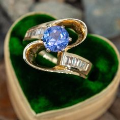 a blue ring sitting on top of a green velvet covered heart shaped box filled with stones