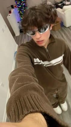 a young man with sunglasses on taking a selfie in front of a christmas tree