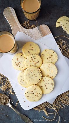 some cookies are on a white plate with two cups of coffee and spoons next to it