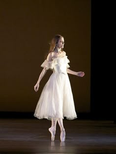 a woman in white dress standing on stage with one leg up and her arms out