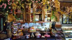 an assortment of desserts and pastries on display in a store with flowers hanging from the ceiling