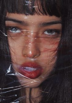 a woman with long black hair and blue eyes is wrapped up in clear plastic covering her face