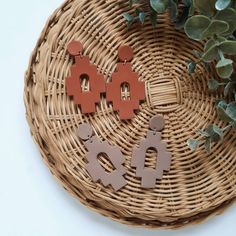 two wooden earrings sitting on top of a wicker basket next to a plant with leaves