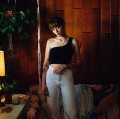 a woman standing in front of a wooden wall wearing white pants and a black top