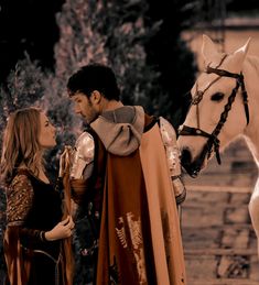 a man and woman standing next to a white horse with a brown cape on it's head