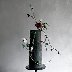 a three tiered black cake with flowers and vines on the top, against a gray background