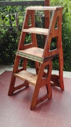 a wooden step stool sitting on top of a red tile floor next to a bush