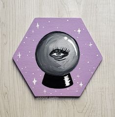 A hexagon shaped canvas painted with acrylics featuring a black and white crystal ball design with an eye in the center. It's surrounded by stars on a muted pastel purple background Simple Fantasy Painting Ideas, Diy Witchy Paintings, Cute Goth Painting, Witch Canvas Painting Diy, Goth Canvas Art, Witch Painting Aesthetic, Pagan Painting Ideas, Witchy Canvas Painting Ideas, Witchcraft Painting Ideas