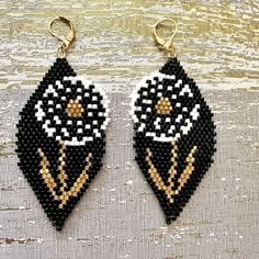 two black and white beaded earrings with gold accents on a wooden surface, one is shaped