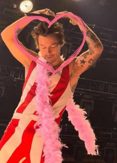 a man in a red and white striped shirt holding a heart shaped object with pink feathers