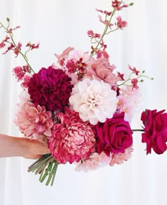 a person holding a bouquet of flowers in their hand with pink and red blooms on it