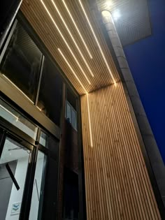 the outside of a building at night with lights on and wood slats covering it