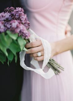 a woman in a pink dress holding a bouquet of flowers and a ring on her finger