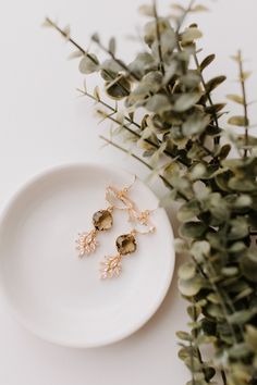 two pairs of gold earrings sitting on top of a white plate next to a plant