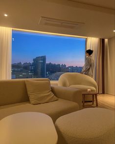 a woman standing in front of a large window looking out at the city from her living room