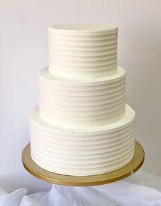 a three tiered white wedding cake on a gold platter