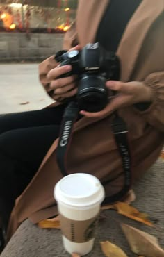 a woman sitting on the ground taking a photo with her camera next to a cup of coffee