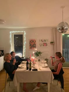 two women sitting at a dinner table with candles on the table and one woman drinking wine