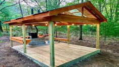 a wooden gazebo sitting in the middle of a forest with lights on it's sides