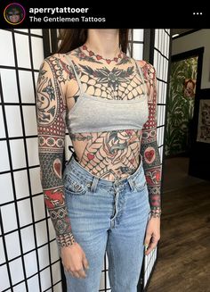 a woman is standing in front of a wall with tattoos on her chest and arms