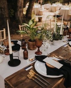 the table is set with white and black plates, silverware, candles and greenery