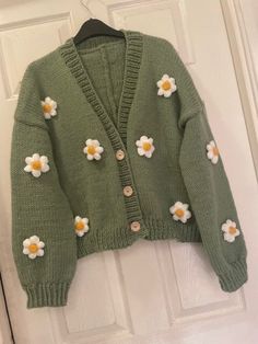 a green cardigan with white flowers on the front and back, hanging from a door