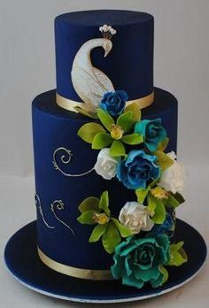 a three tiered blue cake with flowers and a peacock on top