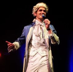 a man in white is singing into a microphone and wearing an elaborate outfit with long sleeves