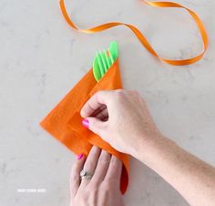 a person is holding an orange piece of paper with scissors in it and some ribbon on the table