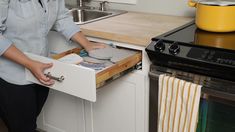 a woman is opening the drawer for her dishwasher and it's next to the stove