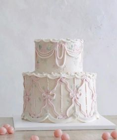 a three tiered cake with pink icing and bows on the top is surrounded by small candies