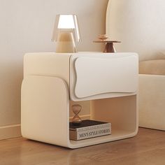 a white table with a book and lamp on it in front of a couches headboard