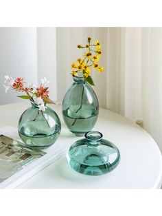 two vases with flowers in them sitting on a white table next to a magazine