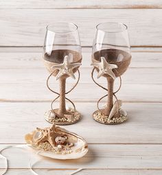 two wine glasses sitting next to each other on top of a wooden table with shells and seashells