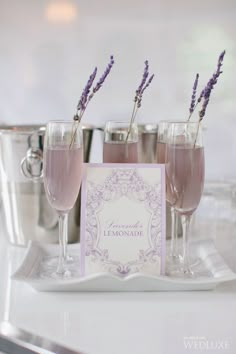 two wine glasses filled with pink liquid and lavender sticks sticking out of the top one