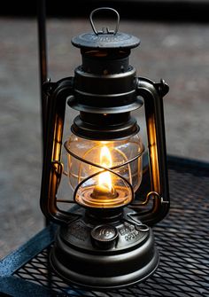 an old fashioned lantern with a lit candle in it sitting on a metal table outdoors