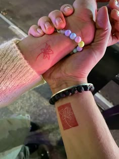 two people are holding hands with tattoos on their arms and bracelets in the other hand