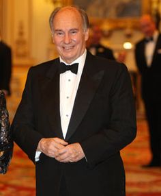 an older man in a tuxedo smiles as he stands next to a younger woman