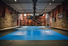 an indoor gym with blue mats and stairs in the center, surrounded by brick walls