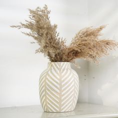 a white vase with some dried plants in it