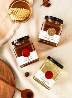 three jars of honey sitting on top of a table next to a spoon and wooden spoon