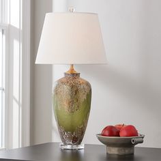 a green vase sitting on top of a table next to a bowl of fruit