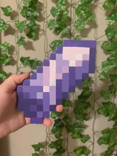 a hand holding a purple piece of paper in front of a wall with green leaves