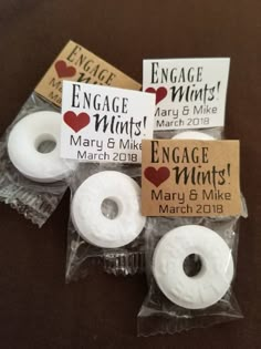 three small white donuts in plastic wrappers with tags on them that say engage mints