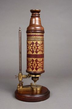 an old fashioned microscope on a stand with a candle next to it and a lighter in the middle