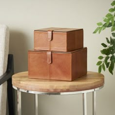 two brown leather boxes sitting on top of a table next to a chair and potted plant