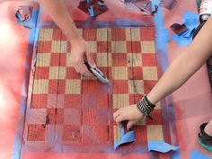 two people are using scissors to cut out wood pieces on a table with red and blue tape